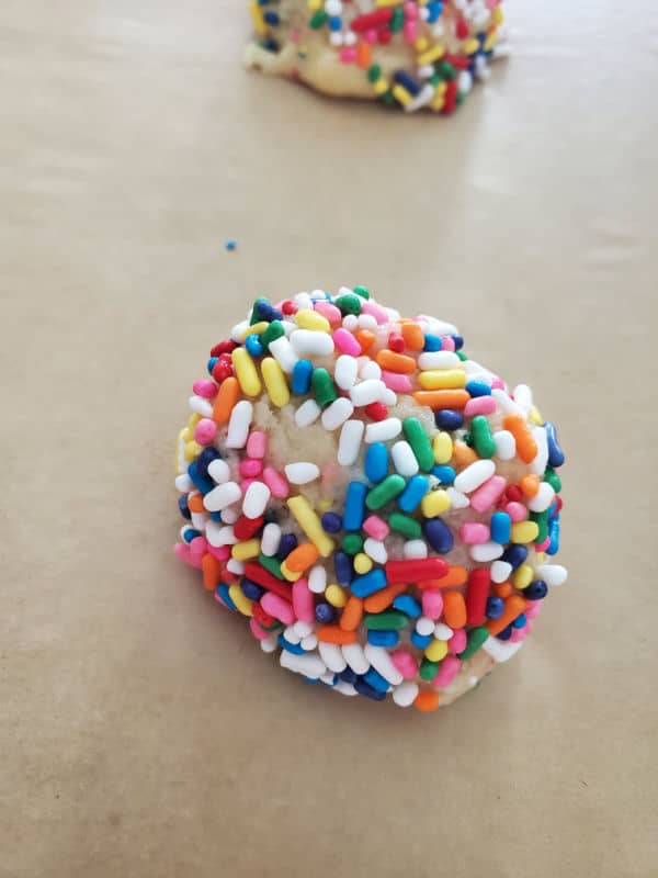 cookie dough ball covered in colorful sprinkles on parchment paper. 