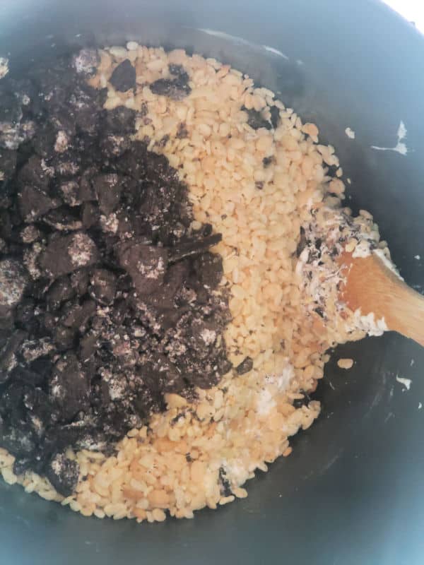 Oreo cookie pieces, Rice Krispie cereal and marshmallows in a pot with a wooden spoon