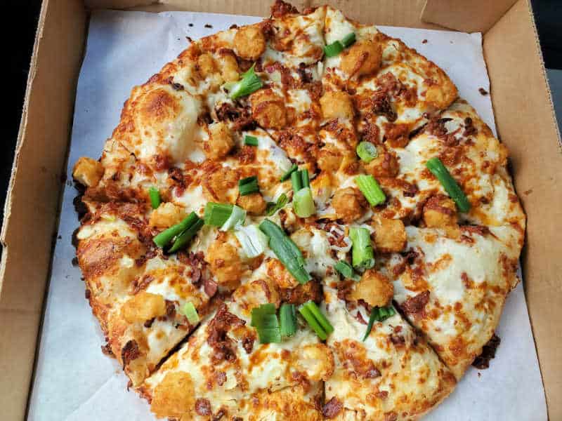 tater tot, green onion, and cheese on a pizza in a cardboard delivery box