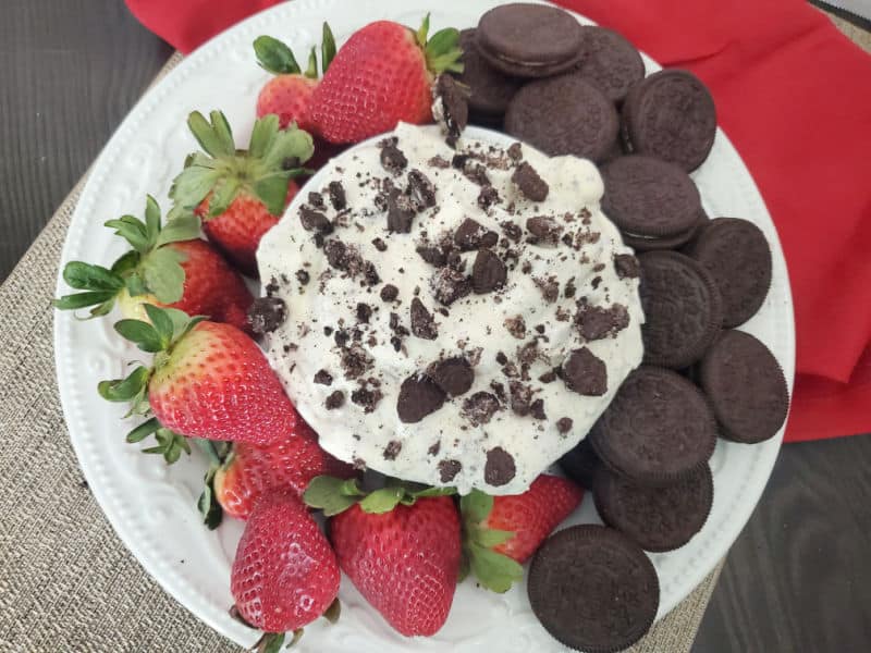 Oreo Cookie Fluff in a white bowl on a white plate with Strawberries and oreo Cookies next to a red napkin