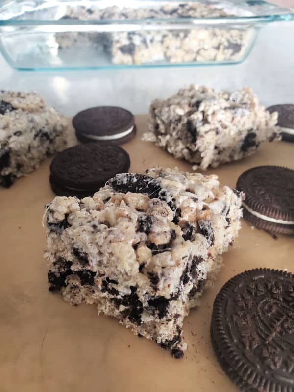 Oreo Rice Krispie Treat squares on parchment paper with Oreo Cookies with a baking dish in the background. 