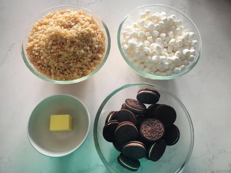Glass bowls filled with rice krispie treats, mini marshmallows, butter, and Oreo cookies