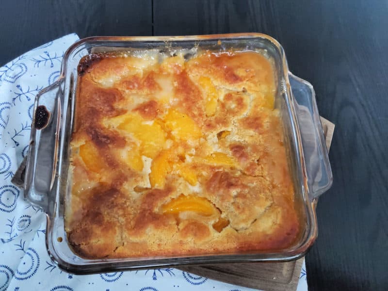 peach cobbler in a glass baking dish on a cloth napkin