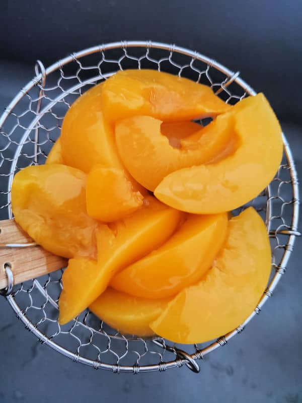 peaches in a spider strainer over the sink 