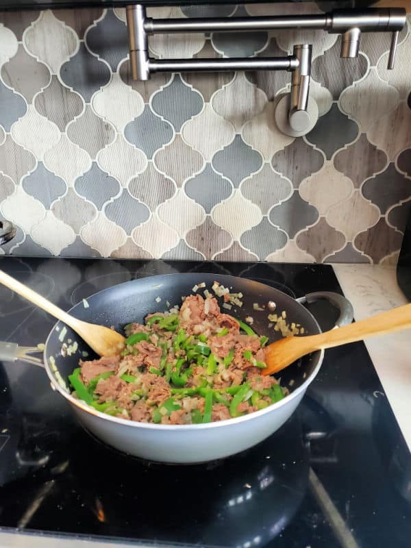 green peppers, onions, and cheesesteak in a skillet on the stove top