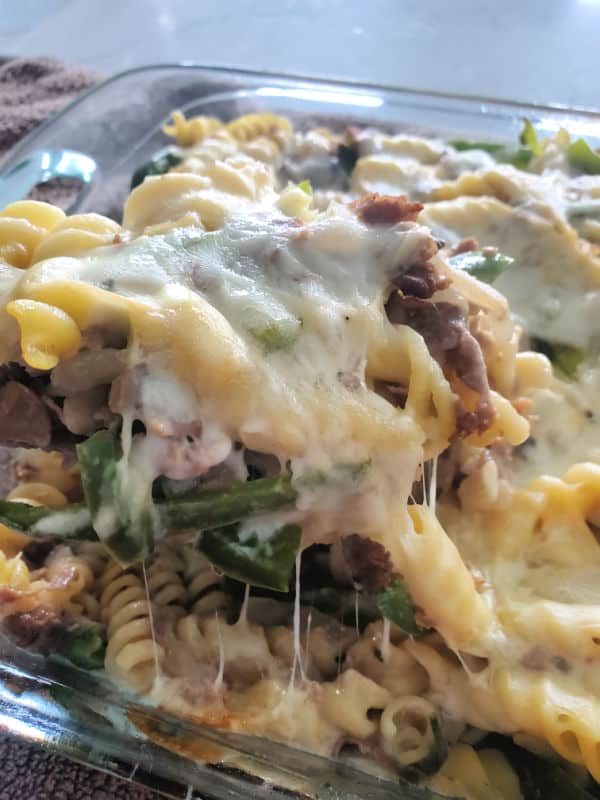 melted cheese over a spoon lifting Philly Cheesesteak casserole out of a baking dish. 