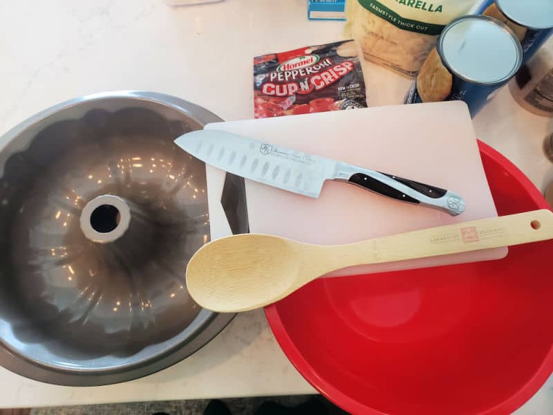 Bundt Pan, Knife, Wooden Spoon, Red Bowl, and cutting board to make Pepperoni Pizza Monkey Bread