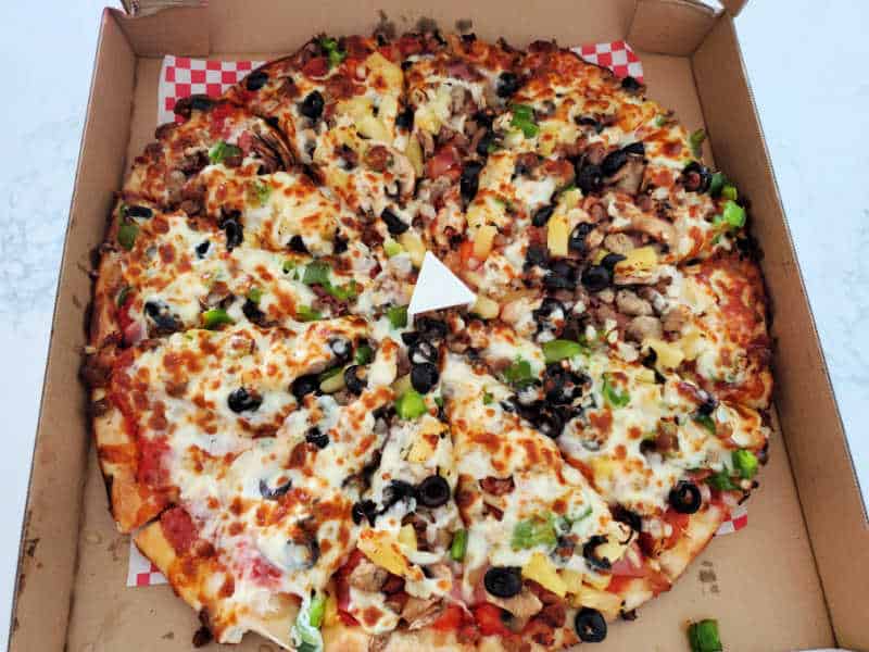 Pizza with cheese, pepperoni, black olives and more in a cardboard delivery box
