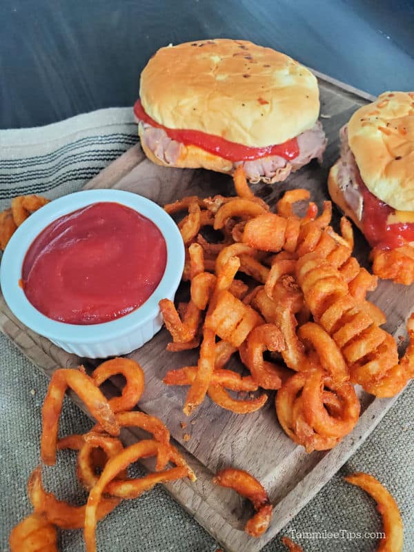 Arby's sauce in a white bowl next to curly fries and two Arby's roast beef sandwiches. 