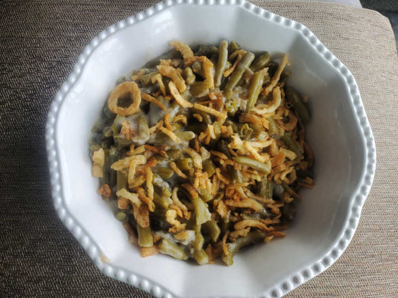 campbells green bean casserole in a white serving bowl on a brown placemat