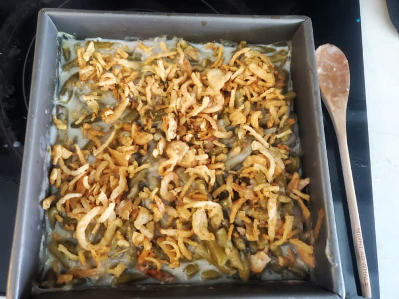 campbells green bean casserole in a baking dish with a wooden spoon next to it