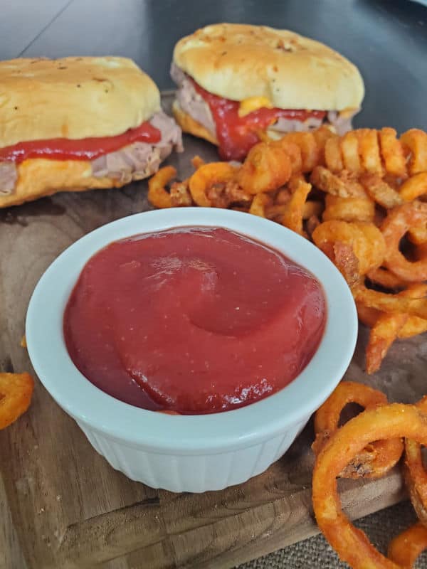 Arby's sauce in a small bowl on a wooden board with curly fries and Arby's roast beef sandwiches 