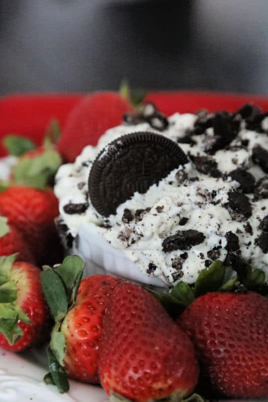 Oreo Fluff salad in a white bowl with cookies and cream garnish next to strawberries