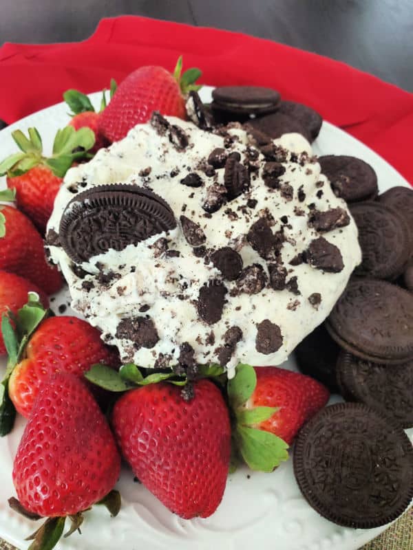 Oreo cookie salad in a bowl next to strawberries and Oreo Cookies with a red napkin