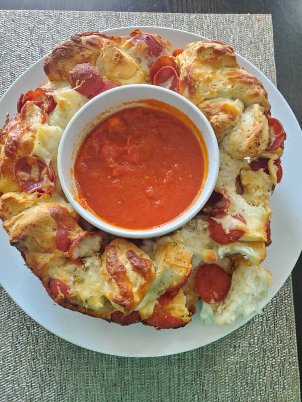 Pepperoni Pizza Monkey Bread on a white circle plate with a bowl of marinara sauce