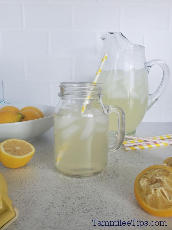 Chick Fil A Lemonade in a mason jar glass with a paper straw next to a pitcher of lemonade and bowl of lemons. 