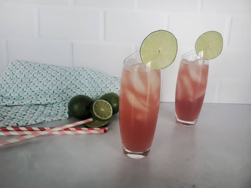 Two bay breeze cocktails on a white counter with straws and limes 