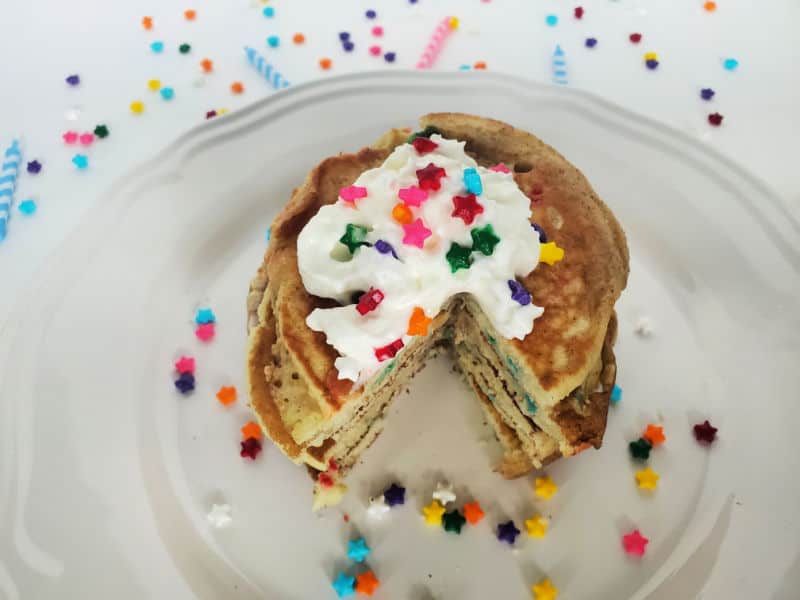 Funfetti Pancakes on a white plate with sprinkles and whipped cream