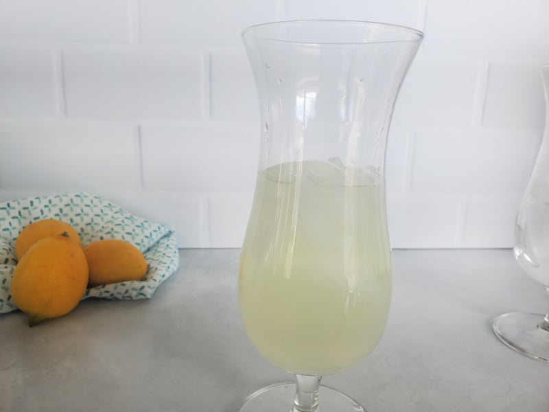 Lemonade in a hurricane glass with lemons in the background