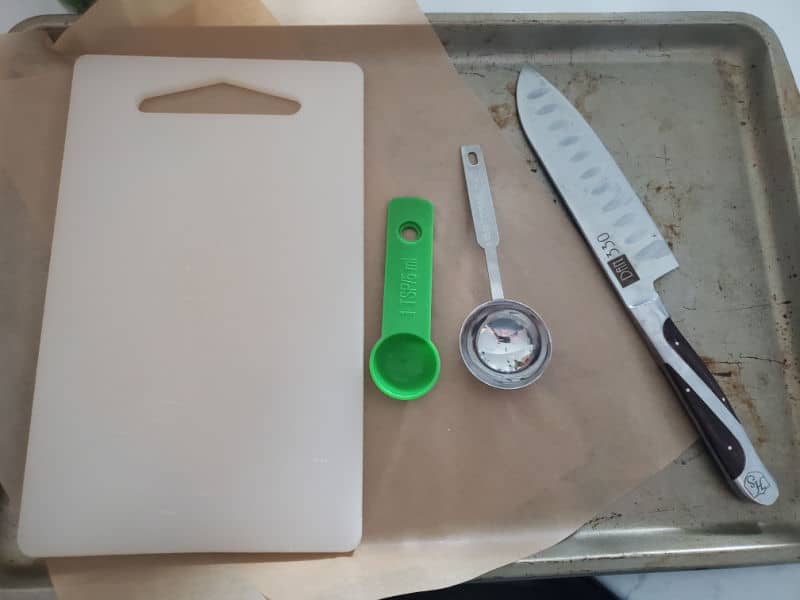 baking sheet with a cutting board, measuring spoons, and sharp knife