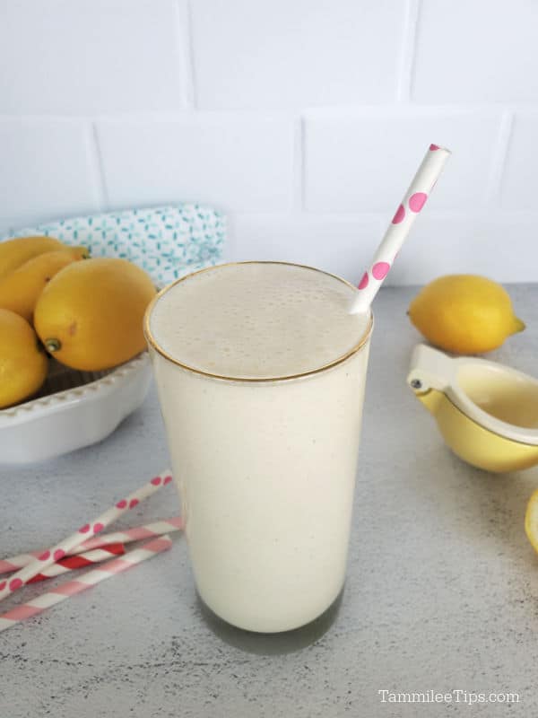 Frosted lemonade in a tall glass with a pink polka dot straw next to a bowl of lemons and more straws. 