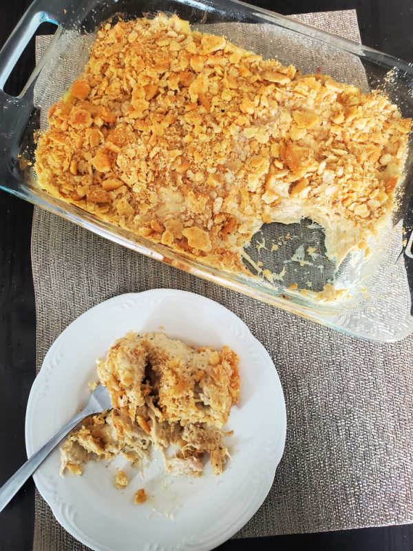 baked ritz chicken casserole in a baking dish next to a white plate with a serving of casserole on it with a fork. 