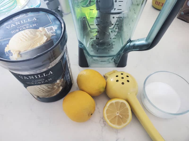 vanilla ice cream, lemons, lemon squeezer, sugar, and a blender on a white counter. 