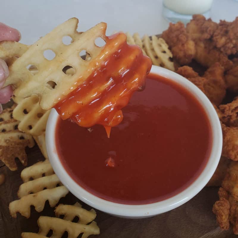 Waffle fry dipping into Polynesian sauce in a white bowl