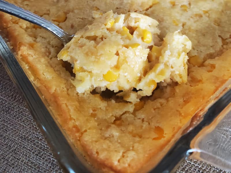 Spoon holding creamed corn casserole out of the glass baking dish