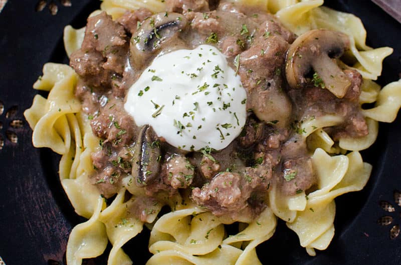 Crock Pot Beef Stroganoff on a blue plate with a dollop of sour cream on top