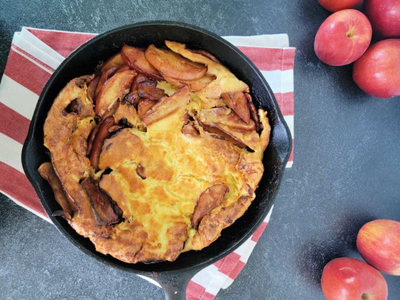 German Apple Pancake in a cast iron skillet on a red striped cloth towel with apples 