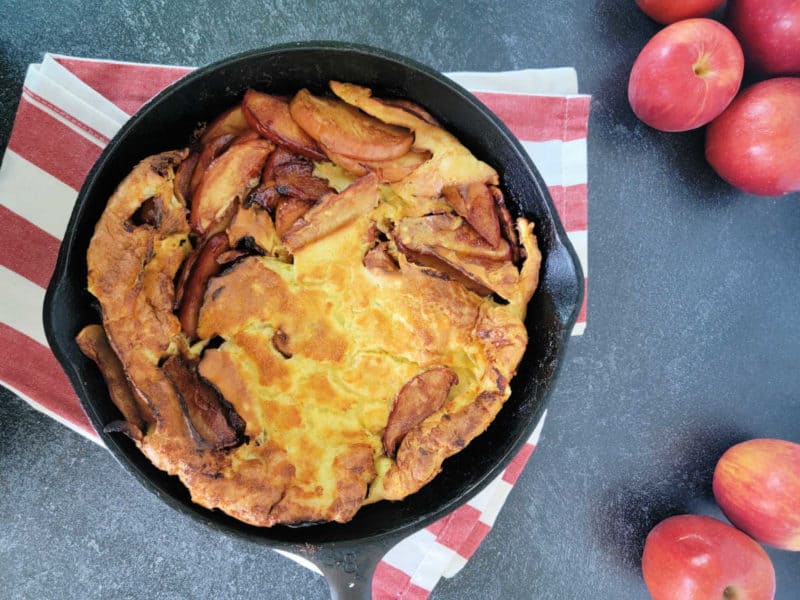 German Apple Pancake in a cast iron skillet on a red striped cloth towel with apples