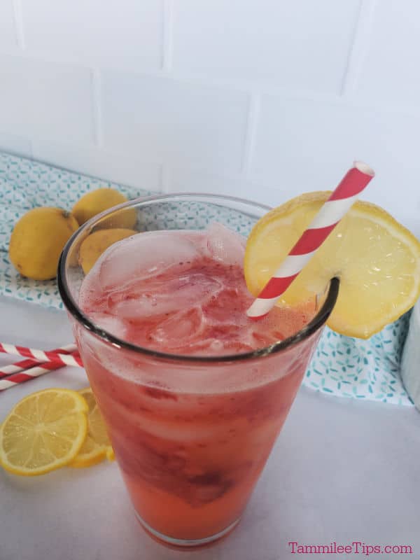 freckled lemonade in a glass with a lemon wheel garnish. lemons and striped straws in the background.