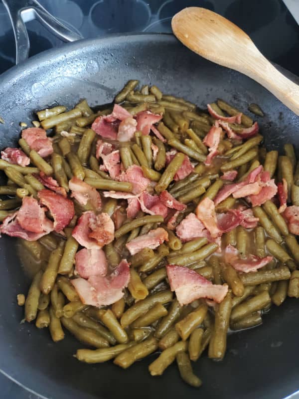 Southern style green beans and bacon in a dark skillet with a wooden spoon on the side