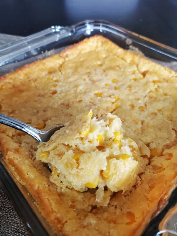 creamed corn casserole being scooped out of the baking dish on a large spoon