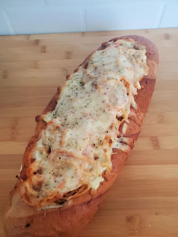 Melted cheese over spaghetti in a loaf of bread