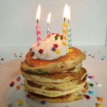 Stack of Funfetti Cake Mix Pancakes on a white plate with lit birthday candles, whipped cream, and sprinkles.