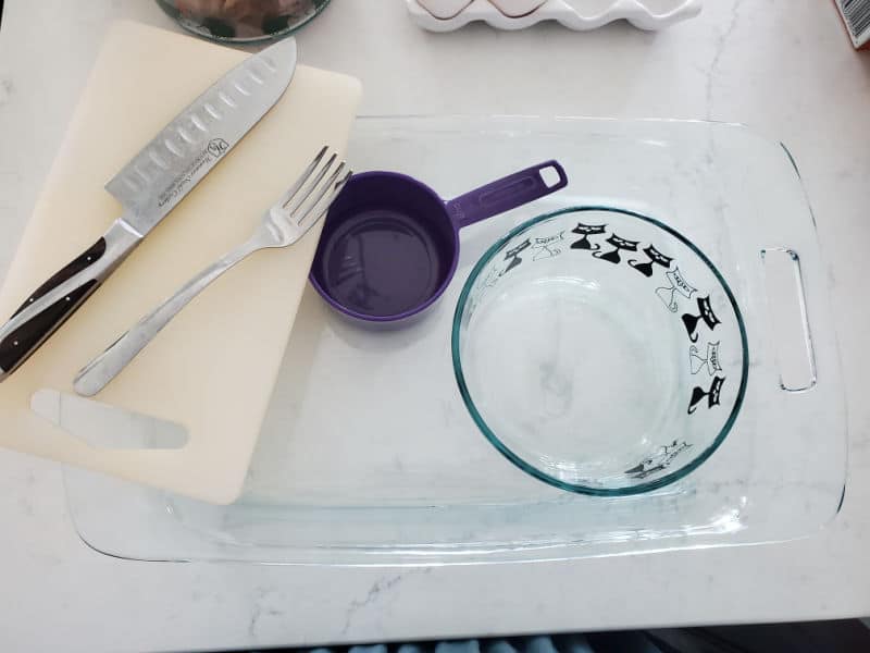 Knife, fork, cutting board, measuring cup, glass bowl, and glass baking dish on a counter. 