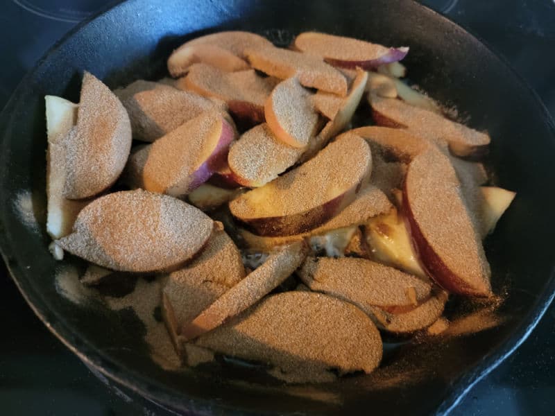 Sliced apples covered in cinnamon for a German Apple Pancake in a cast iron skillet