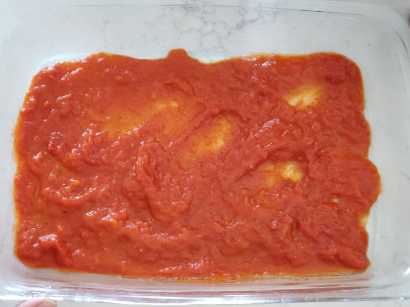 tomato sauce spread in the bottom of a glass casserole dish