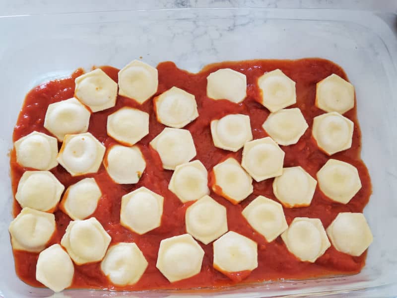 round ravioli spread evenly over marinara sauce in a glass casserole dish 