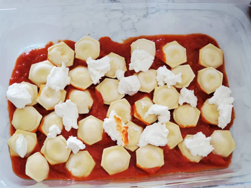 Ricotta cheese over ravioli and marina sauce in a glass casserole dish