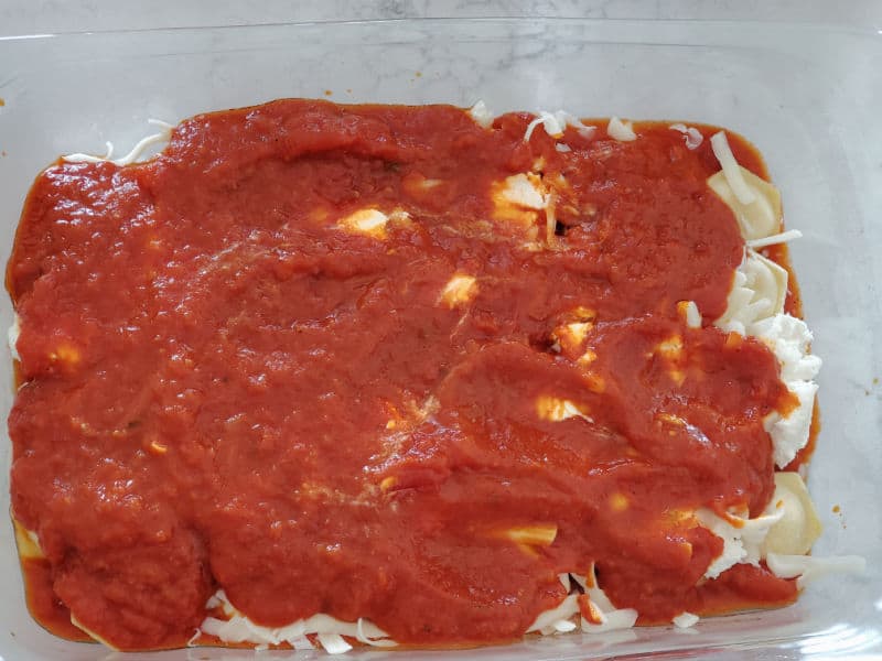 marinara sauce and mozzarella cheese on top of ravioli in a glass casserole dish