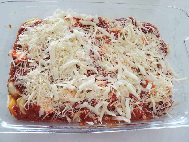 shredded mozzarella cheese over ravioli and marinara sauce in a glass casserole dish