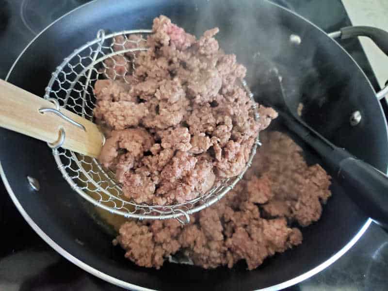 Cooked ground beef in a strainer over a skillet