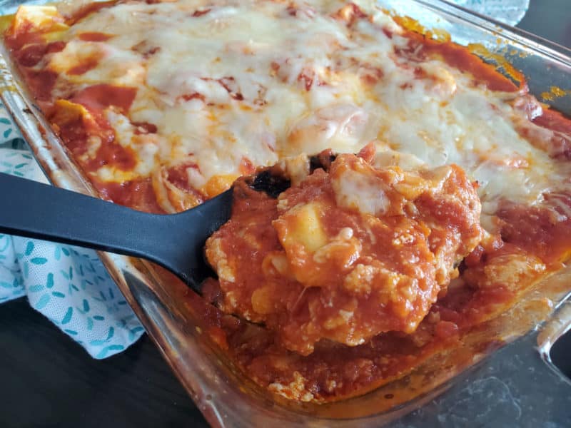 black spoon scooping lasagna from a glass casserole dish