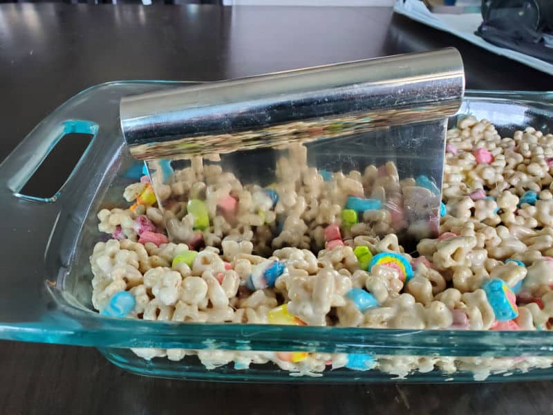Dough scraper cutting into Lucky Charms treats in a glass baking dish