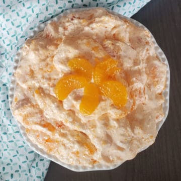 Mandarin Orange Jello Salad in a white bowl with orange slice garnish