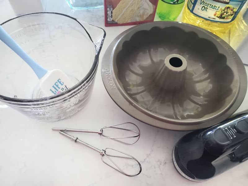 glass bowl with a spatula, bundt cake, whisks, and a hand mixer