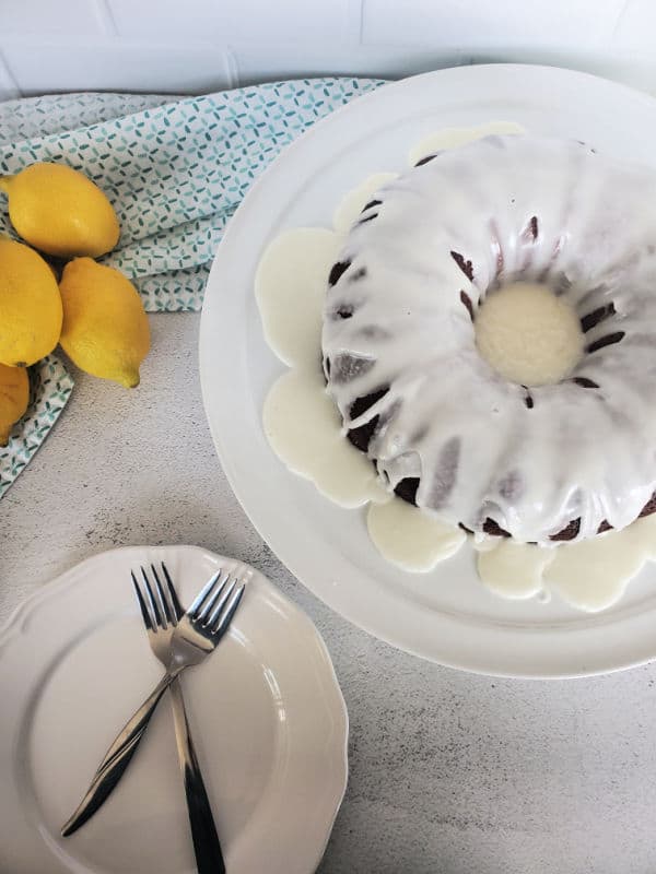 Mountain Dew Bundt Cake on a white platter next to a bowl of lemons, and a plate with forks